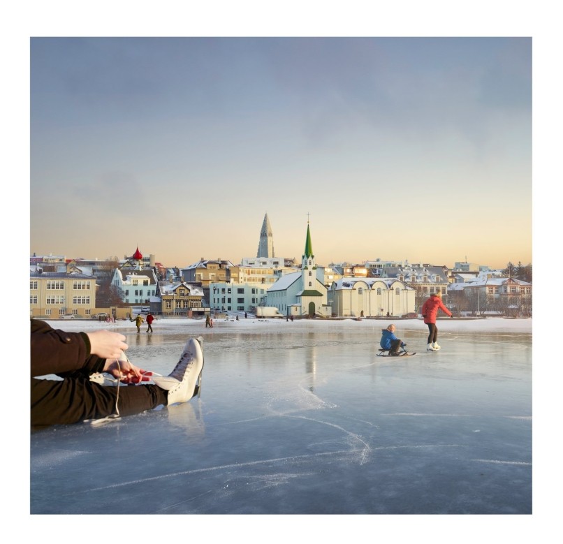 Schaatsers op een bevroren meer in Reykjavik met de skyline van de stad op de achtergrond